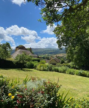 A rural landscape with thatched-roof cottages, lush greenery, and a clear blue sky. - Relaxing retreat in an 1880's Chapel development, coastlines & national parks. (Taunton)