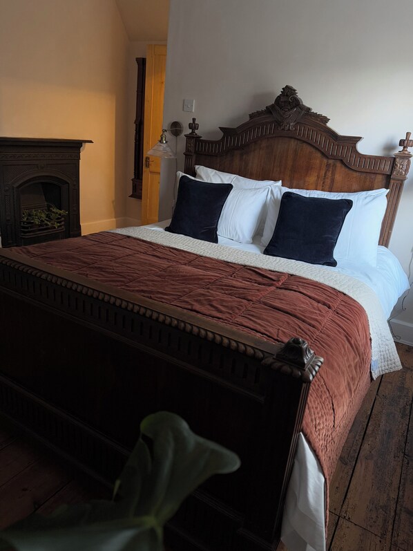Een traditioneel houten bed met een rode sprei, witte lakens en donkere kussens.