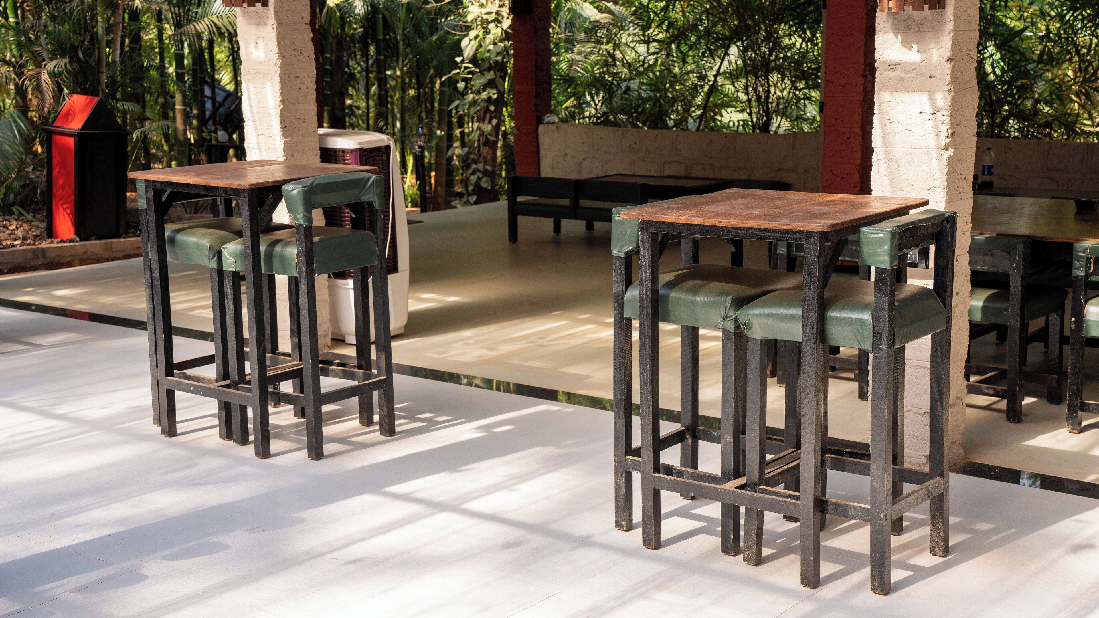 A patio area with high tables and chairs, surrounded by greenery.