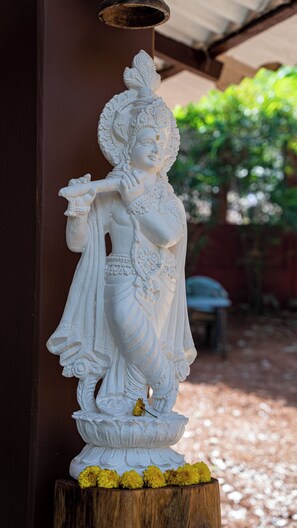 A white statue of a deity with intricate carvings, placed on a wooden base with yellow flowers.
