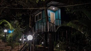 A two-story building with a staircase leading to the entrance, surrounded by dense foliage.