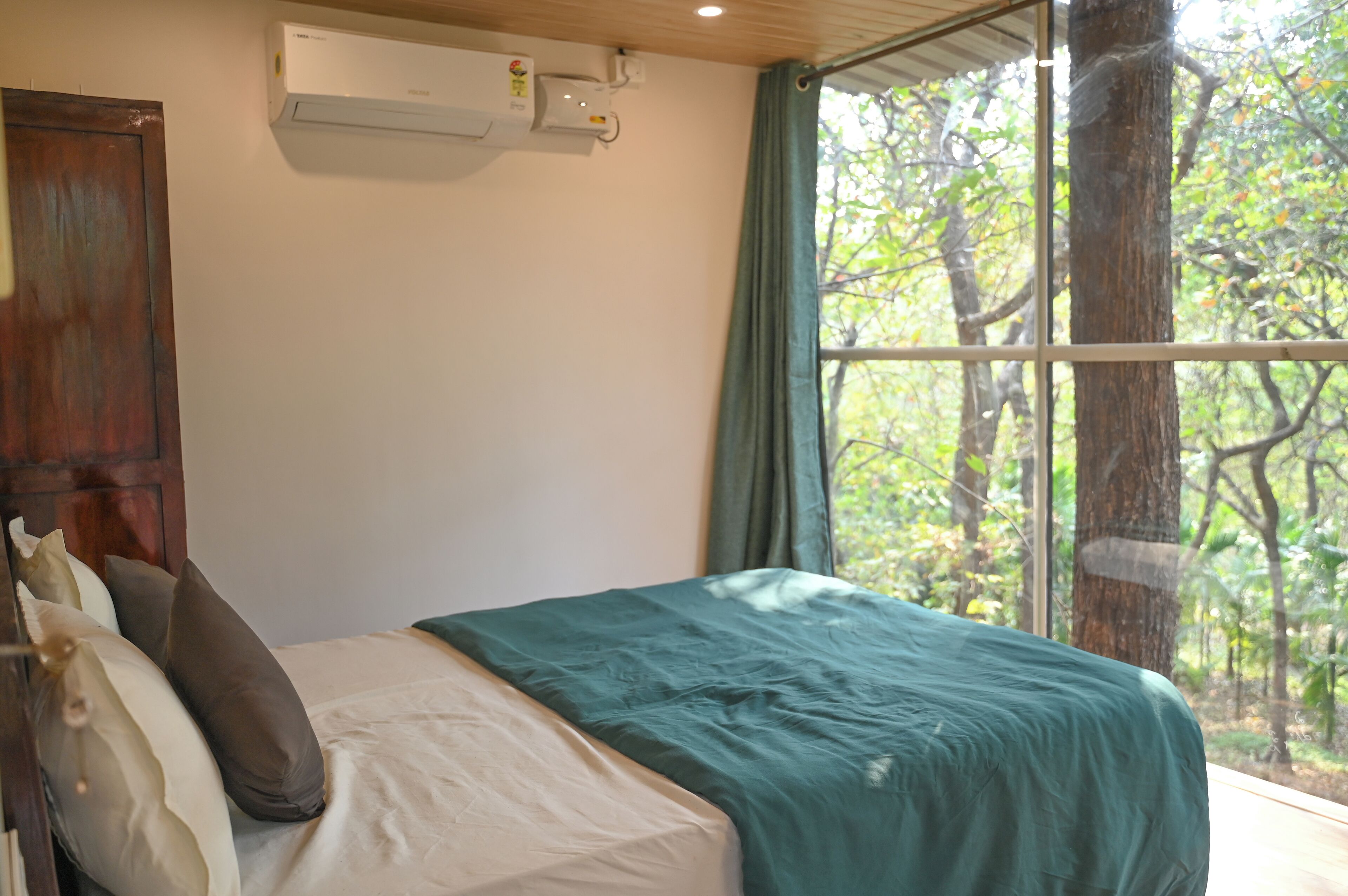 A bedroom with a bed, a window with a view of trees, and an air conditioning unit on the wall.