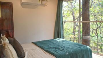 A bedroom with a bed, a window with a view of trees, and an air conditioning unit on the wall.