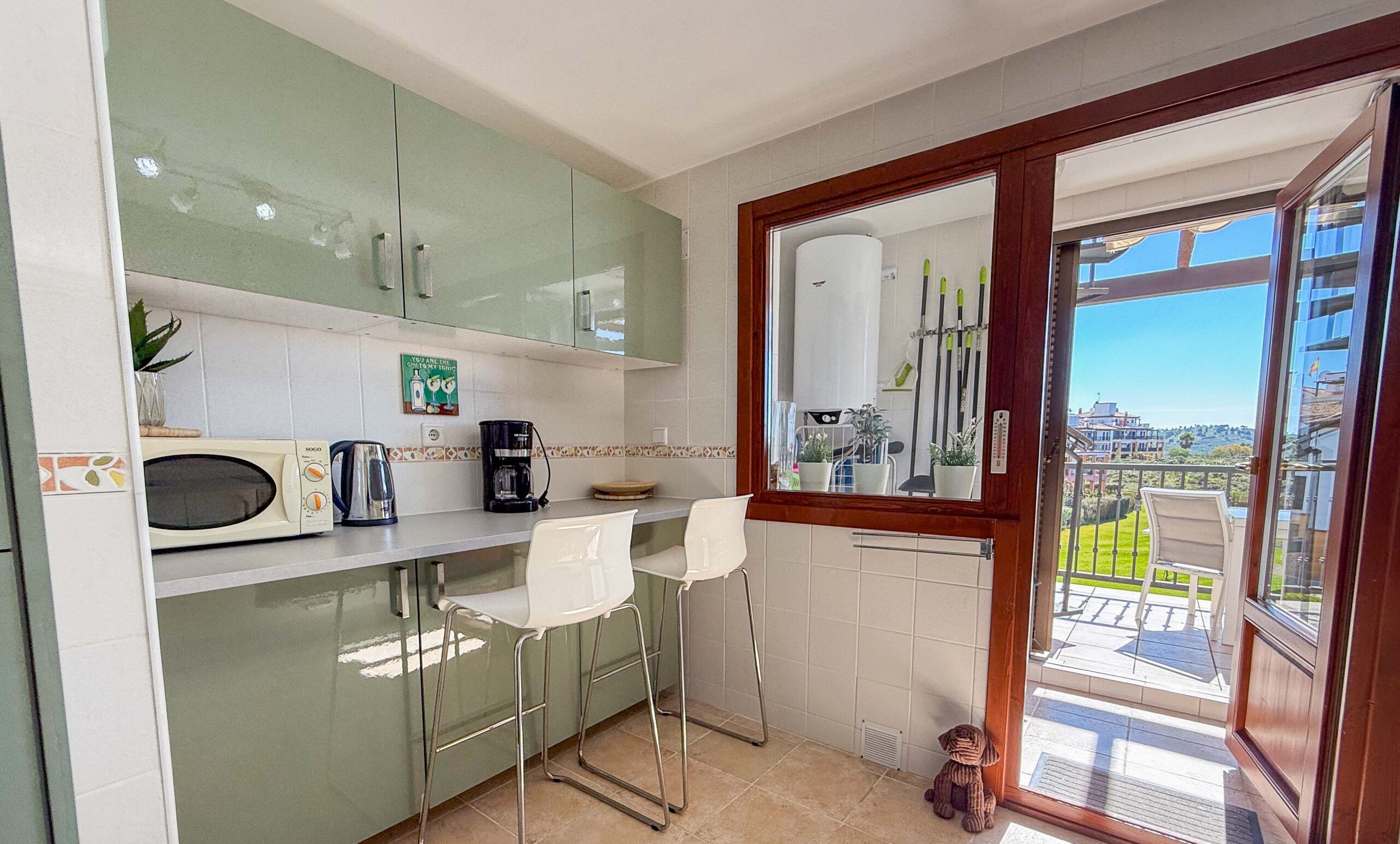 A kitchen with a microwave, coffee maker, and bar stools. There is a window with a view of a balcony and buildings.