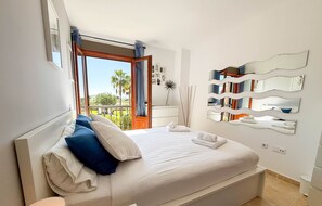 A bedroom with a large bed, a view of palm trees, and a balcony. - Bright Modern Apartment Shared Pool KUC01 (Ayamonte)