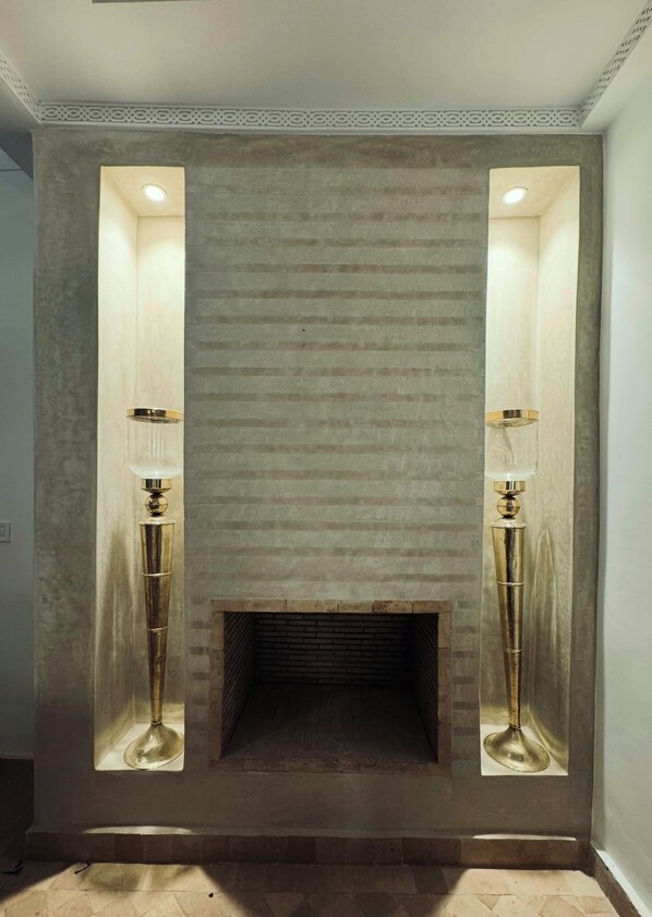 A fireplace with a textured stone surround and two tall, modern-style wall sconces on either side. - Riad in the shade of orange trees. (Marrakesh)