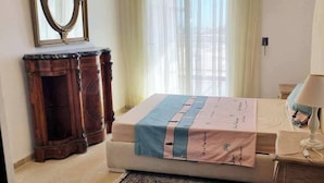 A neatly made bed with a pink and blue blanket, a wooden nightstand with a lamp, and a large mirror on the wall.