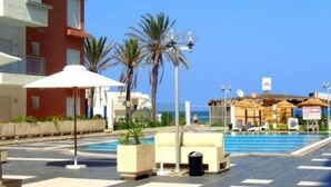 A pool area with lounge chairs, palm trees, and a building with balconies.