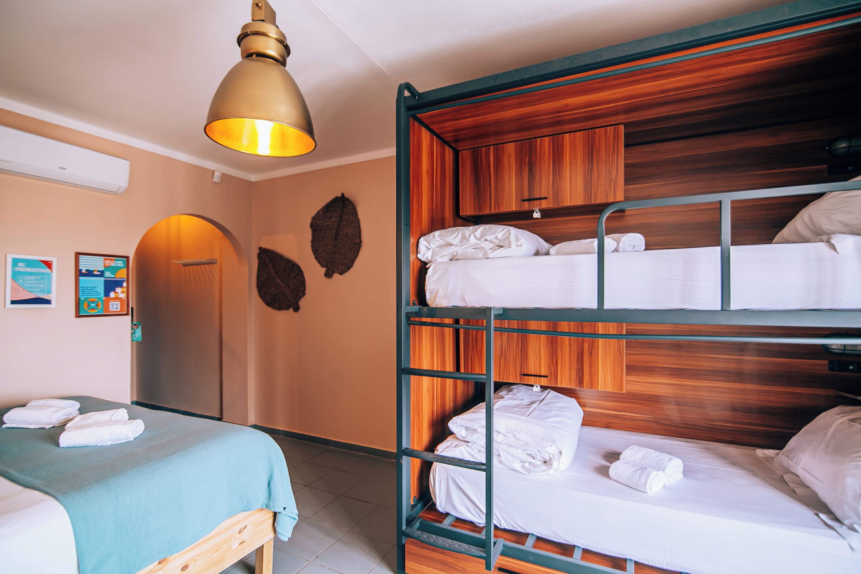 Habitación de hotel con literas, una cama individual, una lámpara de techo y un cabecero de madera.