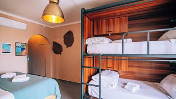 Habitación de hotel con literas, una cama individual, una lámpara de techo y un cabecero de madera.