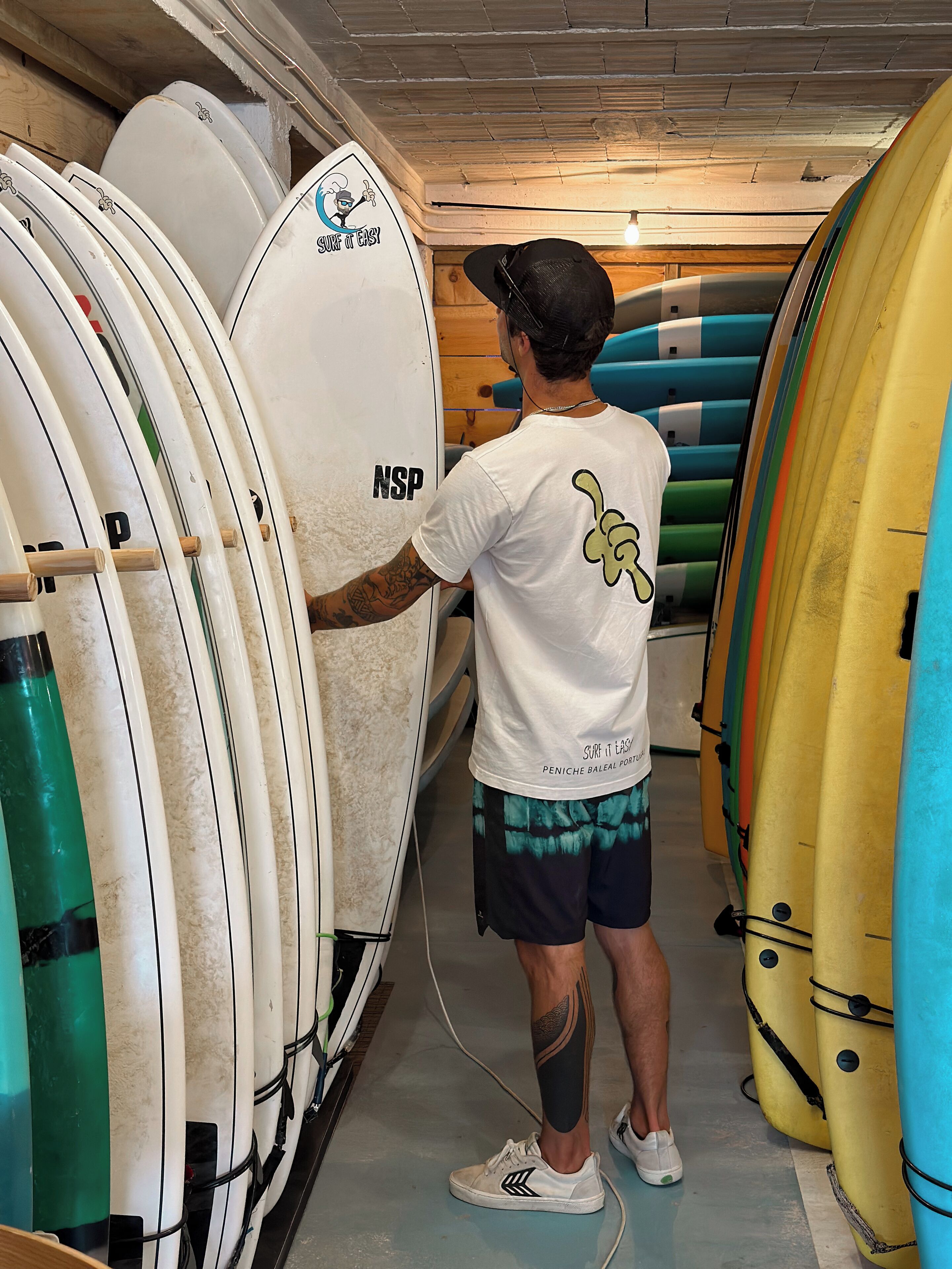 A person standing in a surfboard storage area, surrounded by various surfboards.