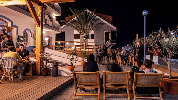 Een terras met rieten stoelen en tafels, een houten terras en potplanten.