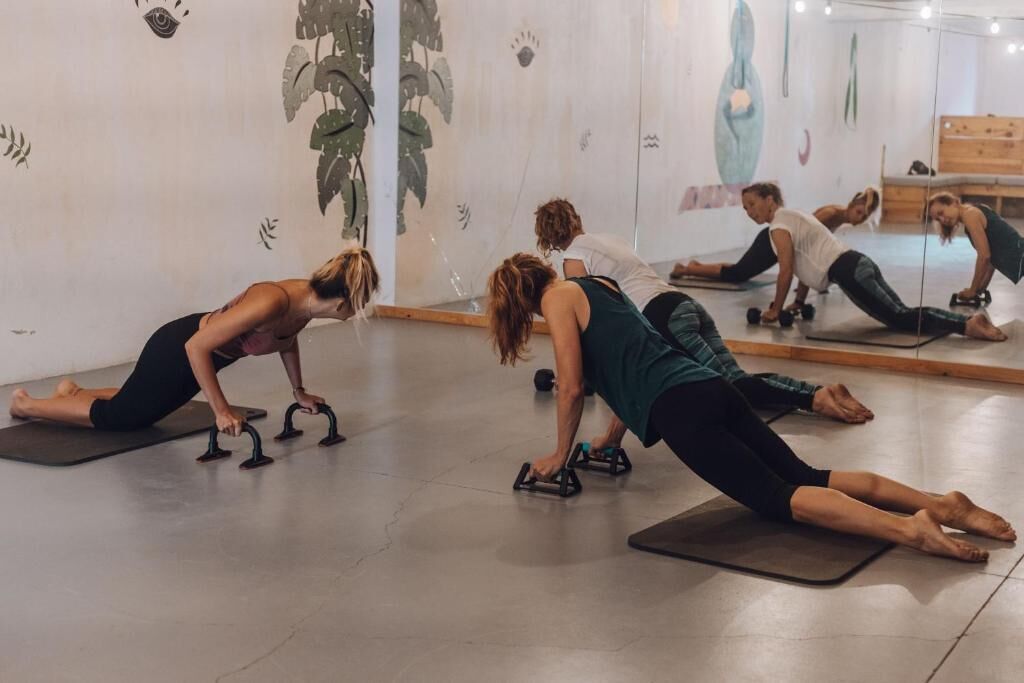 A group of people performing yoga in a room with mirrors and artwork on the walls.