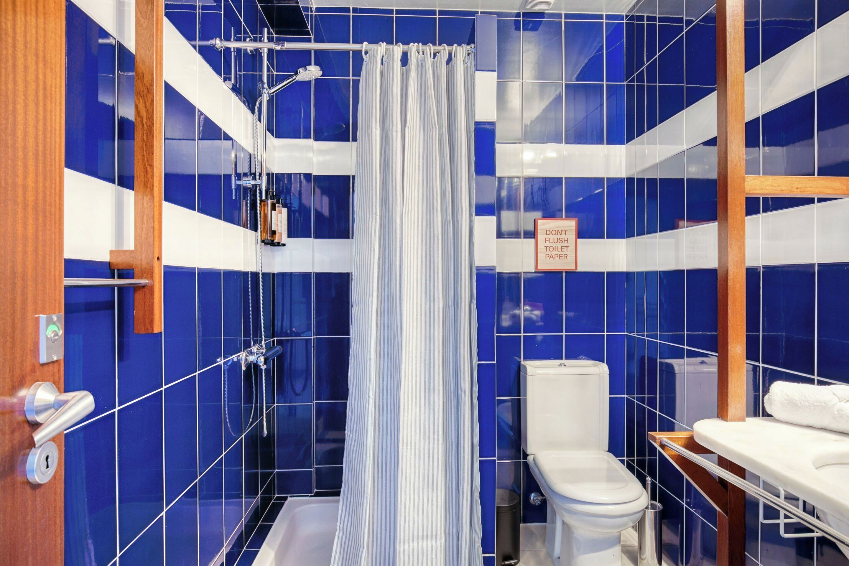 Une salle de bain avec des carreaux bleus, un rideau de douche, des toilettes et un lavabo.