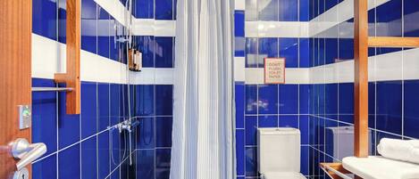 Une salle de bain avec des carreaux bleus, un rideau de douche, des toilettes et un lavabo.