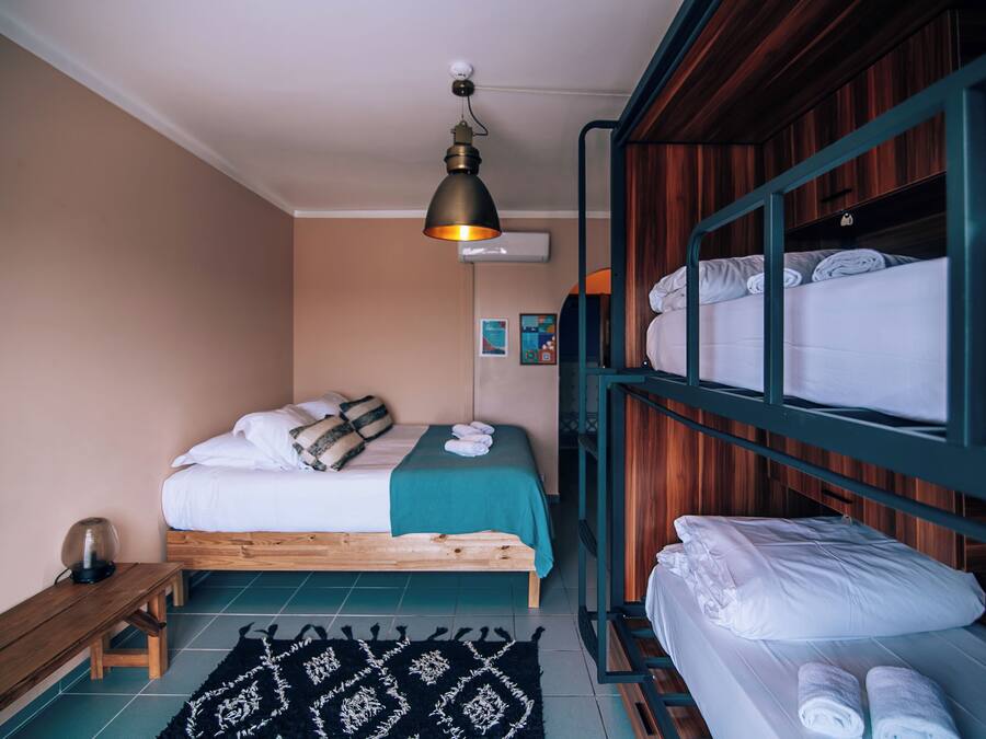 A bedroom with a single bed, a bench, a hanging light fixture, and a bunk bed with towels.