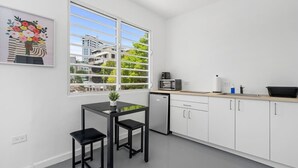 A modern kitchen with white cabinets, a black countertop, a microwave, and a dishwasher. There is a window with a view of buildings and trees. - Otium | Walk to the Beach | Free Local Coffee (San Juan)