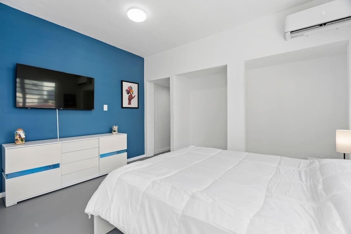 Een slaapkamer met een groot bed, een aan de muur bevestigde televisie, een dressoir en een airconditioning.