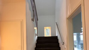A staircase with dark steps leading to a landing, white walls, and a door on the left. - Vacation home in the Alter Hof - charming, central, with garden (Bad Zwischenahn)