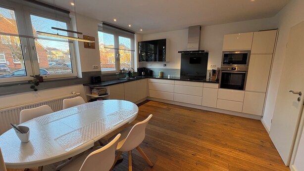 A modern kitchen with white cabinets, a black stove, and a dining table with chairs. - Vacation home in the Alter Hof - charming, central, with garden (Bad Zwischenahn)