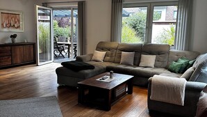 A modern living room with a sectional sofa, a coffee table, and a dining area with a table and chairs. - Vacation home in the Alter Hof - charming, central, with garden (Bad Zwischenahn)