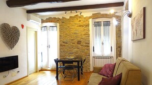 Ein Wohnzimmer mit Steinwand, Holzboden, einer Couch, einem Fernseher und einem Esstisch mit Stühlen.