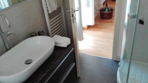 Ein modernes Badezimmer mit einem weißen Waschbecken, einer dunklen Arbeitsplatte und einer Duschkabine aus Glas.