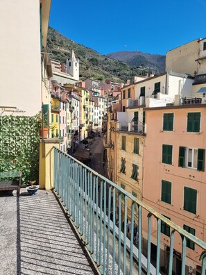 A narrow street with colorful buildings, a church spire, and a hillside in the background. - Apartment in the center of town with magnificent terrace and view of Ligurian houses (Riomaggiore)