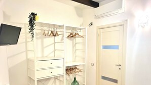 Ein Schlafzimmer mit weißem Kleiderschrank, einem Bett, einem grünen Blumenvasen und einem an der Wand befestigten Fernseher.