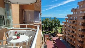 Uma varanda com mesa e cadeiras, com vista para o mar e edifícios próximos.