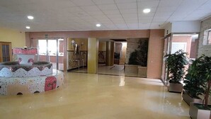 Um hall amplo com piso lustroso, uma fonte decorativa central e plantas em vasos.