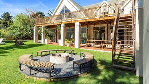Ein Haus mit überdachter Terrasse, Feuerstelle und Gartenmöbeln.