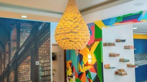 Um interior moderno com arte de parede geométrica, uma luminária pendente e uma estante de livros.