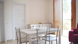 A dining area with a white table and chairs, a wooden cabinet, and a sliding glass door leading to an outdoor area. - Stefy Home (Vaccarizzo-delfino)