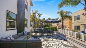 Une terrasse extérieure aménagée avec un canapé, une table à manger et des chaises, le tout entouré d’un tapis à motifs.