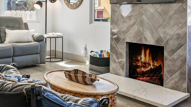 Un salon moderne doté d’une cheminée, d’un téléviseur fixé au mur et d’un coin salon confortable.