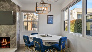 Un coin repas avec une table ronde, des chaises bleues, une cheminée et un lustre.