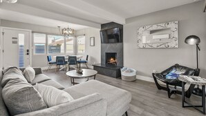 Una sala moderna con chimenea, sofás grises, un comedor y un sillón de cuero negro.