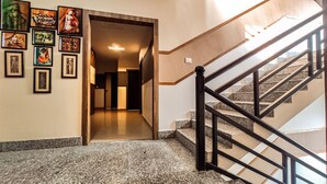 A hallway with a staircase leading to another floor, framed artwork on the walls, and a light fixture above the door. - Hotel Spectrum Residency (Guwahati)