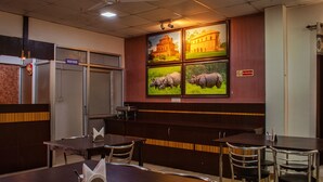 A restaurant with a high ceiling, a ceiling fan, and a wall with four framed pictures. There are tables and chairs, and a sign indicating a wash room. - Hotel Spectrum Residency (Guwahati)
