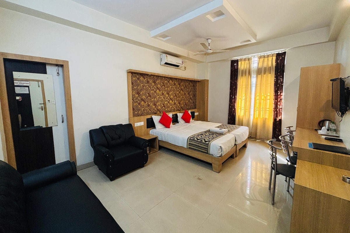 A hotel room with a bed, a black sofa, a desk with a chair, and a television.