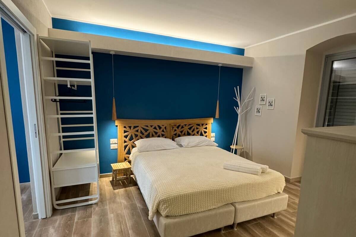 Un dormitorio con cama, cabecero de madera, mesitas de noche, un armario y una lámpara colgante.