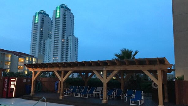 Ein Poolbereich mit Liegestühlen und einer Holzpergola, umgeben von hohen Wohnhäusern.