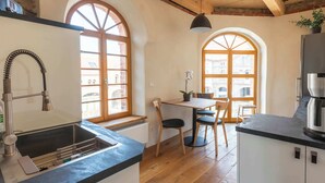 Een keuken met houten balken, een spoelbak, een zithoek met stoelen en een groot raam.