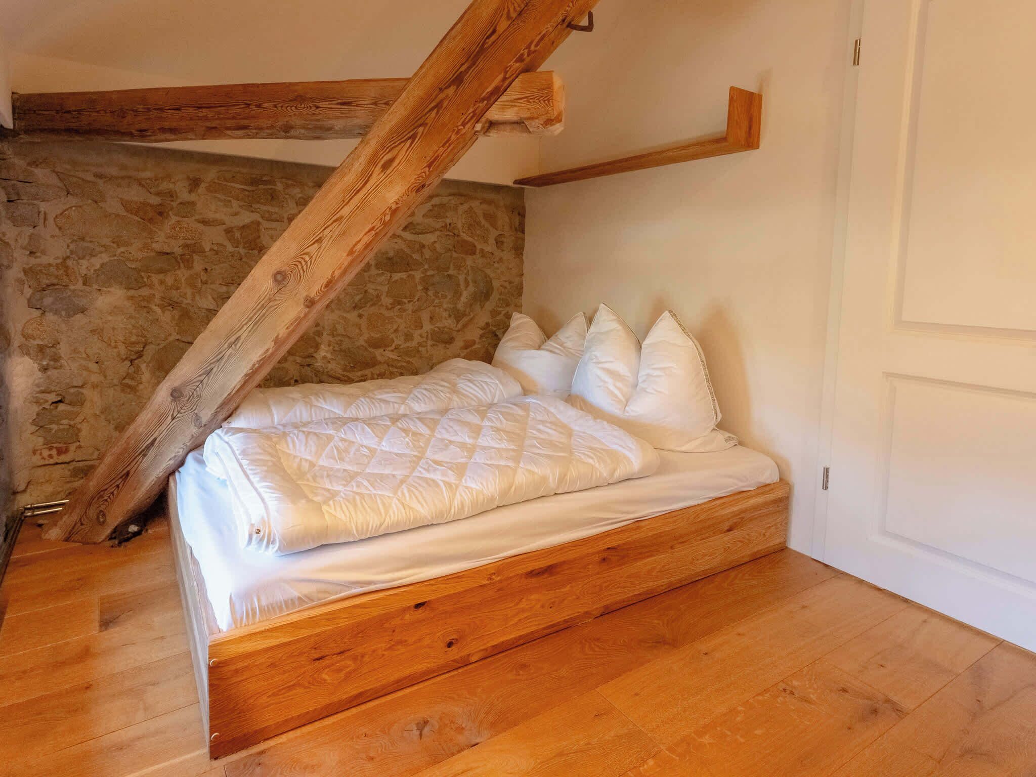 Een slaapkamer met een houten bed, een stenen muur en een schuine plafond.