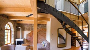 Een loftachtige kamer met zichtbaar baksteen, een houten plafond, een trap en een bank.