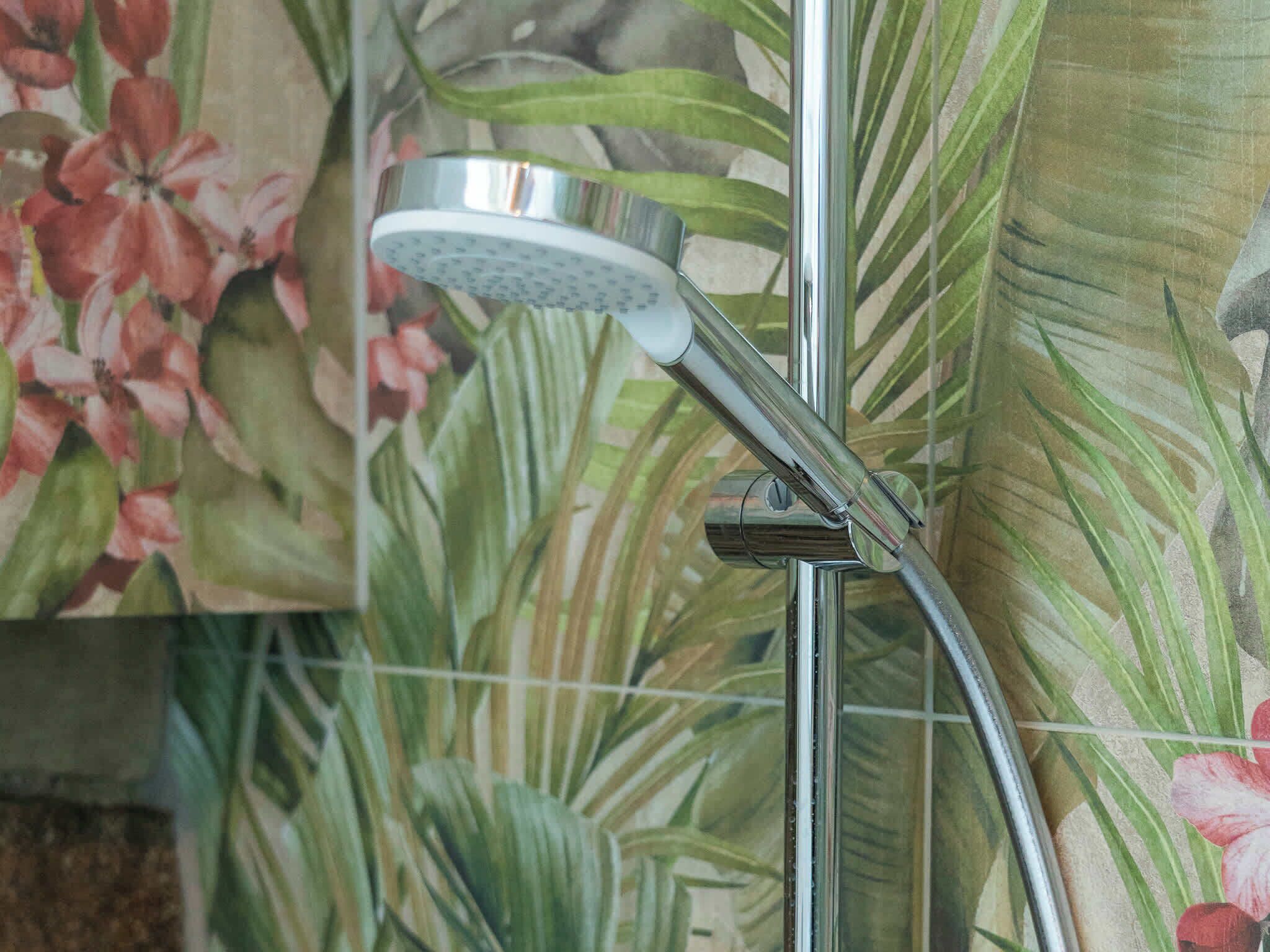Un pommeau de douche fixé sur un accessoire chromé, le tout sur un fond de papier peint à motifs floraux.