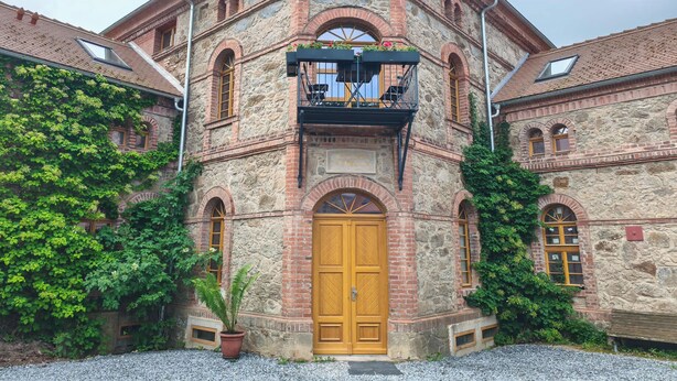 Een historisch gebouw met een opvallende ingang, een balkon met zitplaatsen en een gevel van steen.