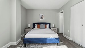 Une chambre à coucher comprenant un lit, des tables de chevet, une œuvre d’art accrochée au mur et une porte.