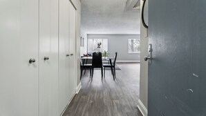 Un couloir mène à une salle à manger où se trouvent une table et des chaises, une plante en pot et une fenêtre donnant sur un paysage.